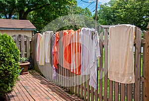 Colorful towels spread opened and hanging on a wooden fence near a backyard swimming pool on a sunny summer day