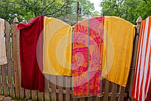 Colorful towels spread opened and hanging on a wooden fence near a backyard swimming pool on a sunny summer day