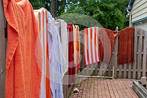 Colorful towels spread opened and hanging on a wooden fence near a backyard swimming pool on a sunny summer day