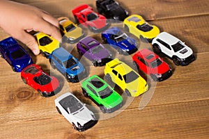 Colorful toy cars side view on a wooden floor background with small child hand holding the toy