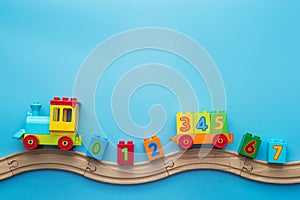 Colorful toy train locomotive with numbers on wooden railway on blue background. Kids toys background banner. Early childhood