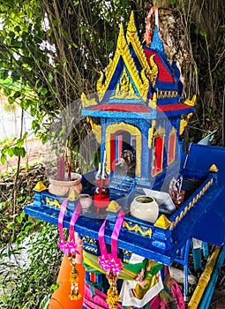 Colorful Traditional Thai outdoor spirit house shrine with flower garlands under the tree shade