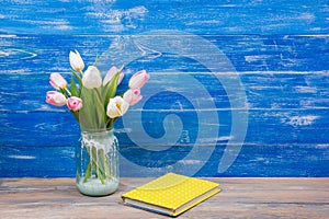 Colorful tulips flowers and yellow book on blue wooden desk table background. Copy space