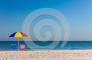 Colorful Umbrella with Pink and Blue Deckchairs on an Empty Beach