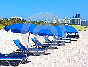 Colorful umbrellas and lounge chairs on Miami Beach with visible city skyline.
