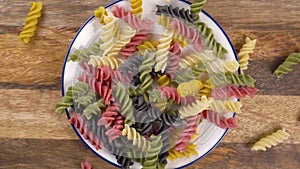 Colorful uncooked fusilli pasta. Italian multicolored macaroni falling in a pile in a plate on a rustic wooden board.