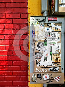 Colorful Urban Brick Building Exterior Wall with Electrical Box and Graffiti Stickers.