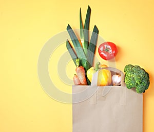 Colorful vegetables in paper bag on yellow empty copy space background.Fresh food,grocery.Healthy nutrition