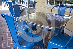 Colorful view of bright blue chairs gathered around a reflective metal table on an outdoor patio at a restaurant
