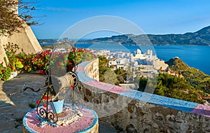 Colorful view on traditional Greek town by sea from decorated terrace with rich red cranesbills. White Orthodox Greek