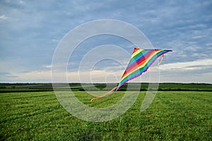 Colorful vivid rainbow kite flying on green field meadow and blue cloudy sky in summer. Family leisure activity. Happy springtime