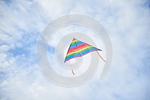 Colorful vivid rainbow kite flying on light blue cloudy sky in summer. Family leisure activity. Happy springtime lifestyle. Child
