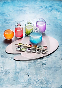 Colorful watercolor paints in glass bottles and the artist`s palette.