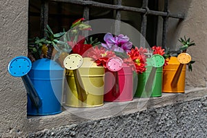 Colorful watering cans on the wall of an old house.