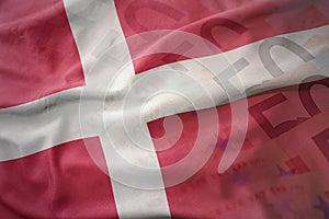 Colorful waving national flag of denmark on a euro money banknotes background.