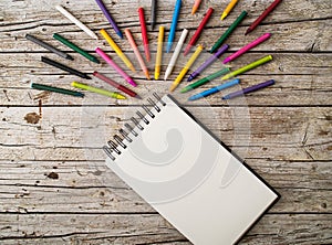 Colorful wax pencils and notepad on wooden background