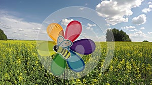 Colorful windmill toy on blossoming rapeseed field, time lapse