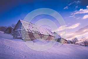 Colorful winter sunrise in the mountains. Fantastic morning glowing by sunlight. View of the snowy forest and old wooden hut cabin