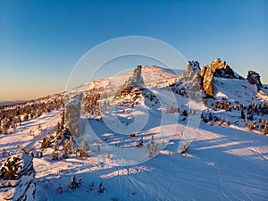 Colorful winter sunset in Sheregesh ski resort mountains with clouds. Aerial top view forest Russia