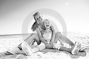 Happy trendy mother and daughter sitting on beach