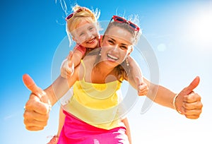 Smiling trendy mother and child on beach showing thumbs up