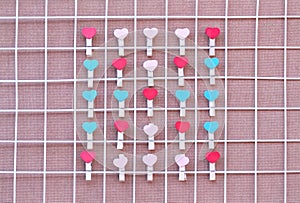 Colorful wooden clothes pins in heart shape patterns hanging on white mesh steel on wood background