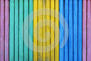 Colorful wooden fence painted in cyan, yellow, blue and purple colors. Multicolored striped texture background.