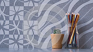 Colorful wooden pencils in glass jar with little green cactus in clay pot on grey tabletop with abstract natural pattern of gray