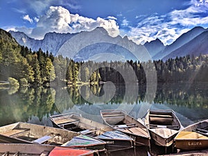 Colorful wooden rowboats on the mirroring lake reflecting the conery trees and mountains behind