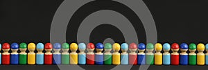 Colorful wooden toy people are lined up in a row or queue, black background with copy space