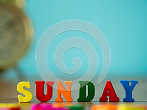 Colorful wooden word SUNDAY on wooden table and vintage alarm clock and background is powder blue. English alphabet made of wooden