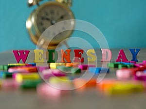 Colorful wooden word WEDNESDAY on wooden table and vintage alarm clock and background is powder blue. English alphabet made of woo