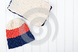 Colorful woolly hat and scarf on white wooden background.