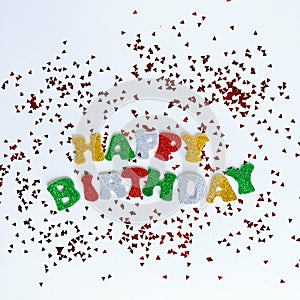 The colorful words HAPPY BIRTHDAY made from multicolored glitter letters on a white background with confetti