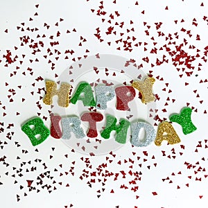 The colorful words HAPPY BIRTHDAY made from multicolored glitter letters on a white background with confetti