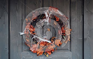 Colorful wreath for halloween hanging on wooden house door made of old orange maple leaves.Spider web.Decorating of porch.Home,