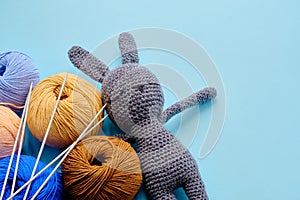 Colorful yarn clews with gray stuffed bunny and needles on the blue background. Concept of amigurumi toy making, handcrafting,