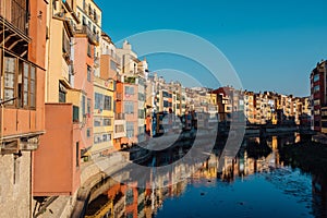 Colorful yellow and orange houses and bridge Pont de Sant Agusti reflected in water river Onyar, in Girona, Catalonia, Spain