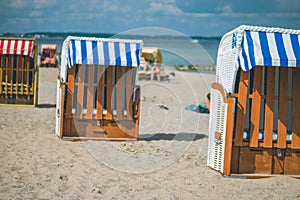 Colorfuled striped roofed chairs on sandy beach in Travemunde. A blurred couple sitting on beach in background. Lubeck