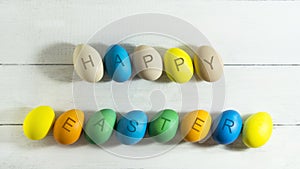 Colorfull eggs with the inscription Happy Easter on a white wooden background.