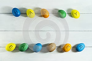 Colorfull eggs with the inscription Happy Easter on a white wooden background.