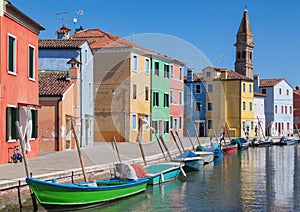 Colorfull facade Houses and bell tower on the island of Burano plus reflection in the water. Waterways with traditional boats