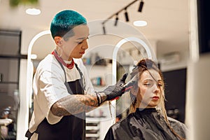 Colorist dyes hair of woman with brush and foil in beauty salon. Professional hair care products