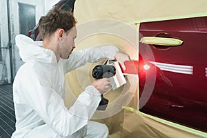 Colorist man compare color sample with car paint using special lamp.