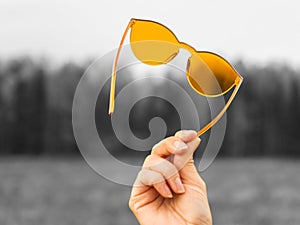 Colorized lifestyle concept. Orange sunglasses in a female hand on a gray background