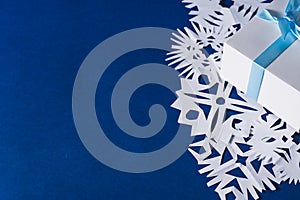 Background of various Christmas themed snowflakes cut out of white paper on a trendy blue background 2020 with a gift