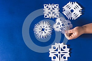 Background of various Christmas themed snowflakes cut out of white paper on a trendy blue background 2020 with a gift