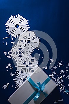 Background of various Christmas themed snowflakes cut out of white paper on a trendy blue background 2020 with a gift