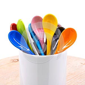 Colors ceramics spoon in mug on wooden backdrops. Colorful concept