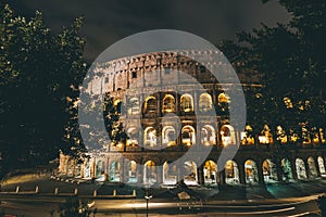 Colosseum surrounded by trees and lights at night in Rome, Italy